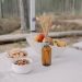 A rustic outdoor table setup featuring a bowl of apples, snacks, and a natural centerpiece amidst a forest backdrop.